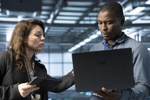 System administrators using laptop in data center, managing server virtualization. IT specialists using notebook in server room, sustaining long term infrastructure reliability photo