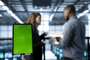 Close up of mockup tablet next to workers in data center using automation tools. Focus on isolated screen tablet in front of technicians in blurry background ensuring continuous uptime of server farm photo