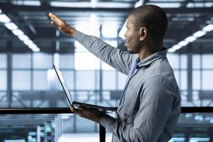 Technician holding laptop, looking around data center, managing server virtualization, finetuning network protocols, verifying high availability configurations, enforcing advanced security measures photo