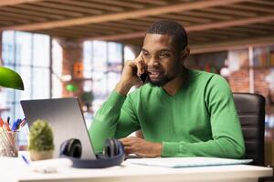 Upbeat man having friendly conversation with friends during telephone call using smartphone. Smiling african american person having fun catching up with mates, talking on phone photo