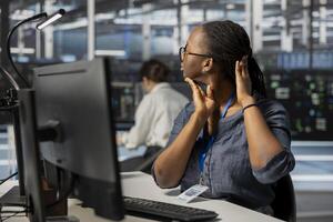 Fatigued data center technician stretching neck while inspecting gear, doing maintenance tasks. Exhausted server farm employee relaxing tensed muscle joints taking break from conducting system checks photo