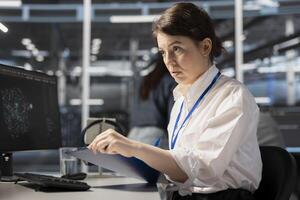Data center admin monitoring system performance using PC, looking over maintenance paperwork. Server farm worker reading documentation files to implement optimizations photo
