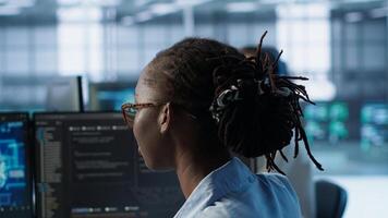 Woman programming in AI data center housing advanced equipment used for machine learning training. African american admin running code to upgrade artificial intelligence tech, camera A close up photo