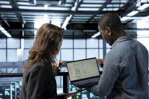 Programmers using laptop in data center, managing server virtualization, running scripts. IT experts using programming language on notebook in server hub, finetuning network protocols photo