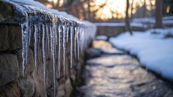 Frozen icicles cascading from a stone wall over a snowy stream. photo