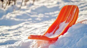 Orange plastic sled rests on a snowy incline. photo