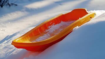 Orange plastic sled resting on a snow-covered hill. photo
