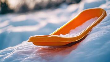 Orange plastic sled resting on a snowy slope. photo