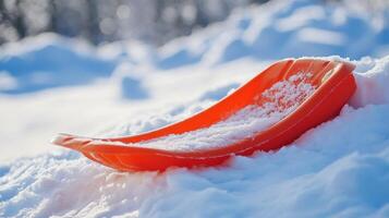 Orange plastic sled resting in snow-covered landscape. photo