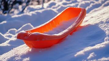 Orange plastic sled rests on a snowy slope. photo