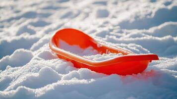 Empty red plastic sled resting on a snowy surface. photo