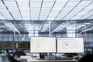 Code running on computer displays in empty data center workspace, used for troubleshooting rackmounts. Binary script running on desktop PC monitors upgrading mainframes systems in server room photo