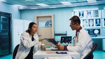 Specialist and patient discussing diagnostic results in a modern medical office, establishing advanced technology to present x ray imaging results and MRI scans. Health care management. Camera B. photo