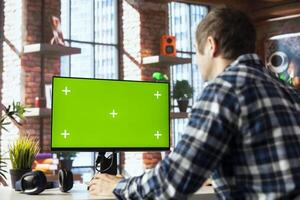 Employee seated at home office desk using green screen PC, checking emails displayed on screen, reading messages in inbox. Man managing electronic correspondence on mockup computer photo