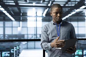 Computer scientist in data center uses tablet, verifying compliance of racks. IT expert in high tech facility optimizing resource utilization, maintaining stable infrastructure using device photo