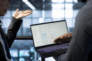 Software developers using laptop in data center, managing server virtualization. IT expert coding on notebook in server room, finetuning network protocols, enforcing advanced security measures photo