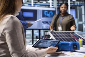 Photovoltaics factory researching team monitoring system performance using tablet. Solar panels plant management executives tracking energy production using device software photo