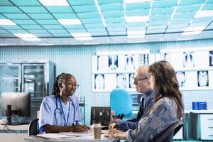 African american nurse evaluating lab test results and discussing potential recovery plan with senior couple, professional patient interaction at the facility. Examination results and analysis. photo
