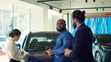 Clients arriving in car dealership, being greeted by friendly car salesman ready to showcase available vehicles to clients. Customers walking in showroom, being welcomed by agent, camera A photo