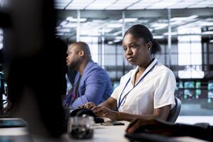African american admin next to colleagues doing yearly checkup to prolong data center electronics life span and avoid downtime. Woman in server hub monitoring server infrastructure components photo