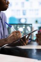 African american nurse takes notes during consultation with old people, creating the healthcare records with symptoms and other problems. Ensuring an easy recovery plan, clinical setting. Close up. photo