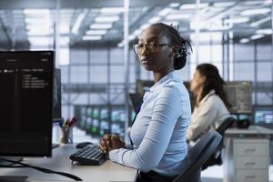 African american engineer managing and optimizing data center infrastructure for maximum efficiency and uptime. Woman in server room maintaining optimal system performance, performing backups photo