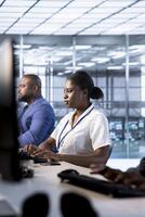 African american admin in data center using PC to check for server performance issues arising due to high CPU usage. Woman in server hub fixing insufficient memory errors slowing down hardware photo