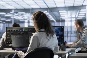 IT staff member programming in AI server farm housing advanced equipment used for machine learning training. Woman running code on laptop to upgrade artificial intelligence rigs photo