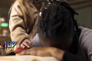 Colleague trying to wake up black student in the university library, girl falling asleep on her stack of borrowed books after studying all night. Sleepy overwhelmed person napping. Close up. photo