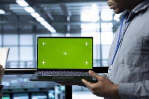 Employees in data center using isolated screen mockup laptop, integrating green technologies. IT experts in server room using chroma key notebook to implement sustainable energy solutions photo