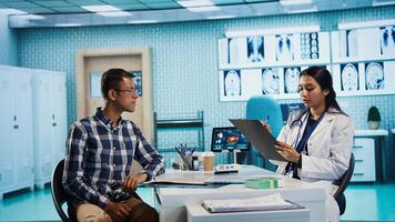 Healthcare provider consulting male patient and reviewing x ray test results, utilizing technology for accurate analysis and patient care management in a medical environment. Camera B. photo