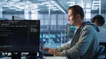 Man working in server hub capable of processing vast amounts of data. IT programmer at PC desk typing on keyboard, updating servers controlling network resources, camera A photo