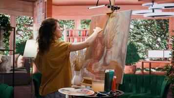 Woman artist wiping off a color from her paintbrush before mixing oil paints, creating multicolored rustic artwork with paint tubes. Painter showing talent and creativity in art studio. Camera B. photo