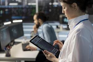 Close up of engineer using tablet in data center, managing server virtualization, running scripts. IT specialist using programming language on device in server hub, finetuning network protocols photo