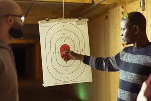 Shooting gallery worker explaining how to hit targets to clients using proper technique. Firing range professional pointing bullseye, teaching man how to shoot with handguns photo