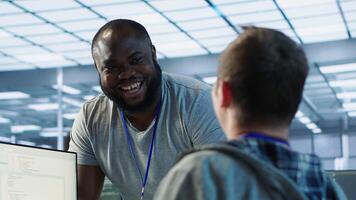 Engineer having fun with colleague at work in data center establishment, making jokes. Team of technicians making each other laugh, bonding in server room, doing fist bump gesture , camera A photo