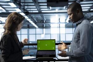 Engineers in data center using isolated screen mockup laptop, inspecting server clusters, updating network topologies. Teamworking IT specialists using chroma key notebook, ensuring stable operations photo