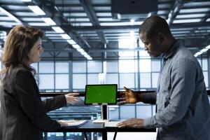 Software developers in data center using mockup tablet, observing analytics, reviewing equipment health. Server hub IT professionals talking, using chroma key device, adjusting system parameters photo