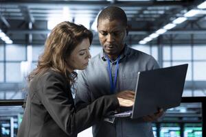 System administrators in data center automating routine maintenance tasks with laptop, executing diagnostic scripts. Server hub IT specialists talking, using notebook to adjust power settings photo