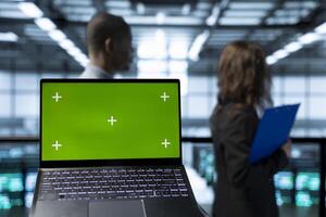 Focus on isolated screen laptop in front of engineers in blurry background doing network virtualization. Close up of mockup chroma key notebook used by admins in server farm verifying settings photo