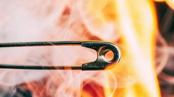 Intense fire action macro shot of a burning safety pin rising smoke trails and orange glow captured in close-up photo