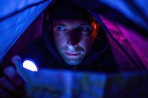 Backpacker reading map with flashlight in dark tent creating warm glow on face night adventure camping experience photo