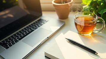 A laptop notebook pen and steaming tea offer a cozy and productive workspace setting photo