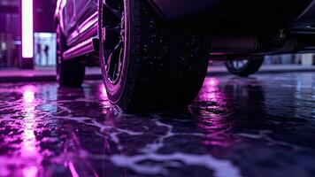 Low angle shot of a car tire on wet surface with vibrant purple and pink neon reflections photo