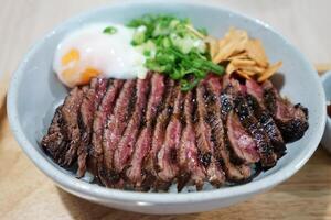 Close up sliced medium rare Wagyu beef served on rice and topped with poached egg and crispy garlic photo