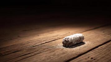 Single chocolate dessert roll dusted with powdered sugar on rustic wooden surface in dramatic lighting photo