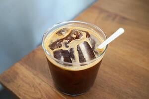 Glass of iced black coffee with plastic straw on wooden table photo