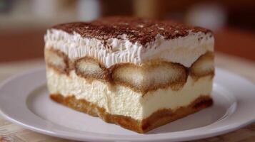 Creamy dessert layer with mascarpone, coffee, and cocoa powder on a white plate in a blurred kitchen background photo
