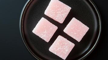 Four pieces of pink sugar on a black plate photo