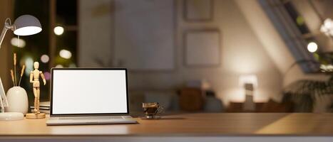 A white screen laptop on the wooden table in lamp light, with the blurred background of dim light room. photo
